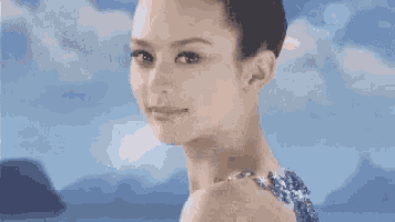 a woman in a blue dress is standing in front of a body of water and mountains .