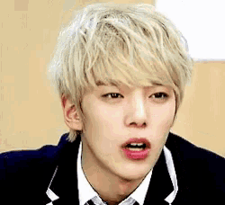a young man with blonde hair and pink lips is wearing a suit and tie and making a funny face .