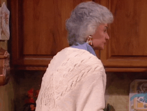 a woman in a white sweater is standing in front of a wooden cabinet .