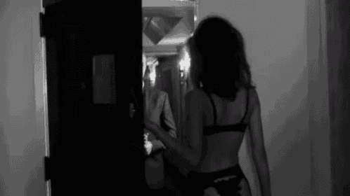 a black and white photo of a woman in lingerie standing in front of a door .