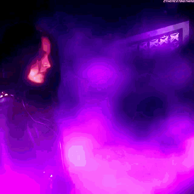 a person standing in a dark room with purple lights behind them