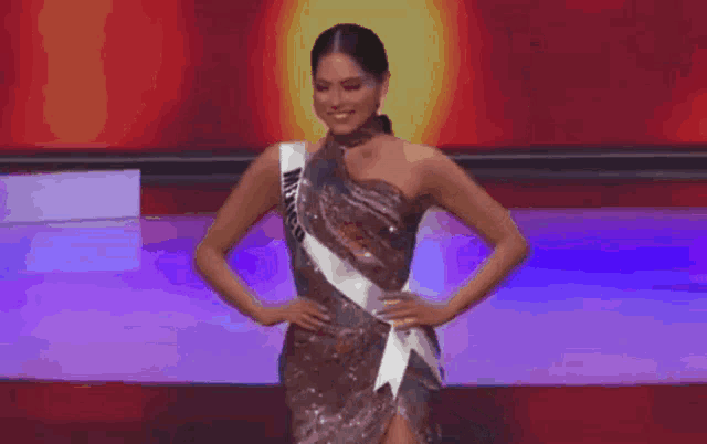 a woman in a dress with a sash around her neck is standing with her hands on her hips