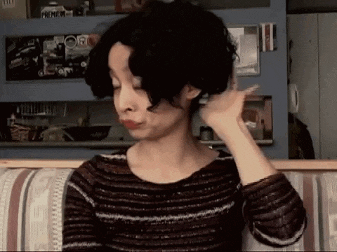 a woman with short curly hair is sitting on a couch and making a funny face .