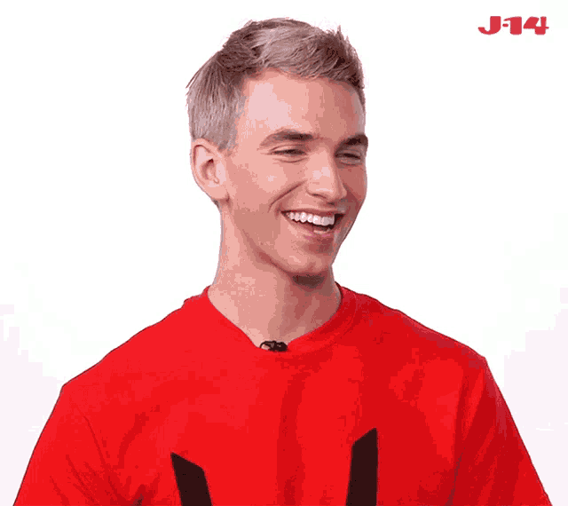 a man wearing a red shirt is smiling with the j14 logo in the corner