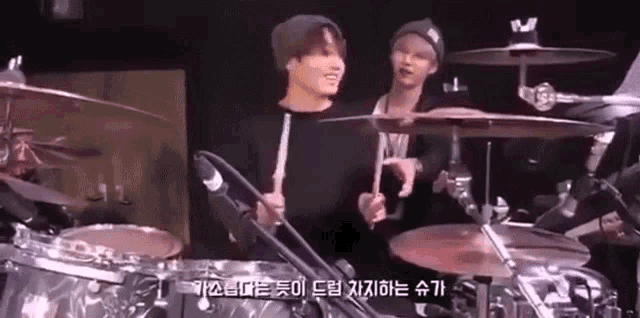 a man is playing drums on a stage while another man watches .
