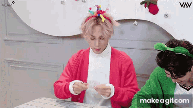 a man in a red jacket is sitting at a table next to another man in a green cardigan ..