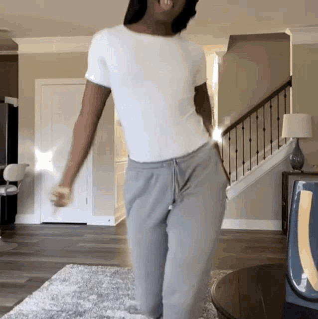 a woman in a white shirt and grey sweatpants is dancing
