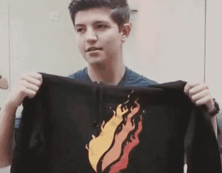 a young man is holding up a black hoodie with a fire design on it .