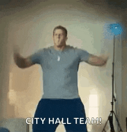 a man is dancing in a room with the words `` city hall team '' written on the screen .