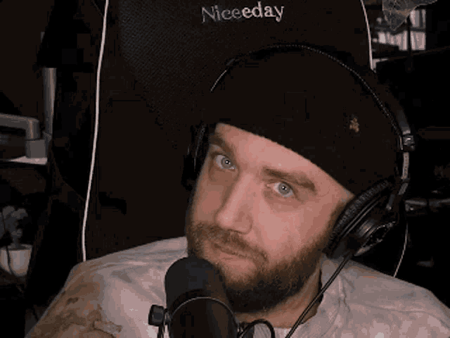 a man with a beard is wearing headphones and a hat while sitting in a chair .