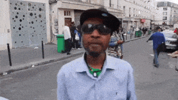 a man wearing sunglasses and a hat stands on a busy street