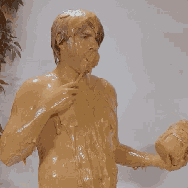 a naked man is covered in brown liquid and holding a hammer