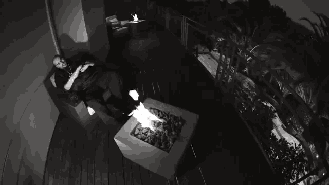 a black and white photo of a man laying on a couch next to a fire pit