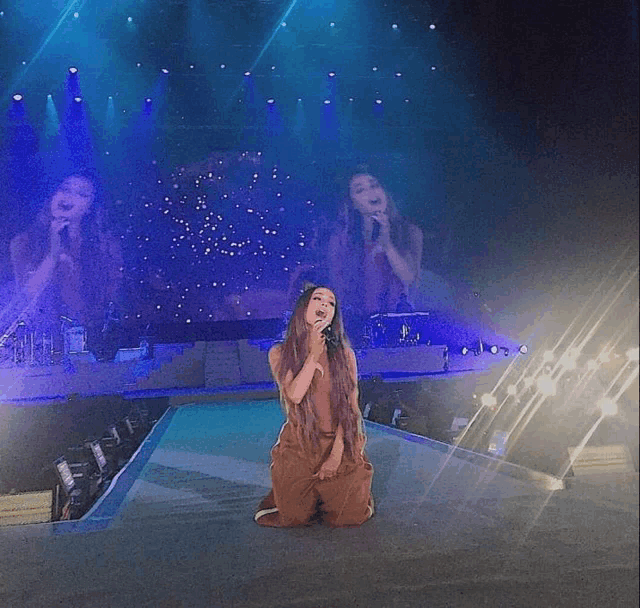 a woman kneeling down on a stage with a microphone in her hand