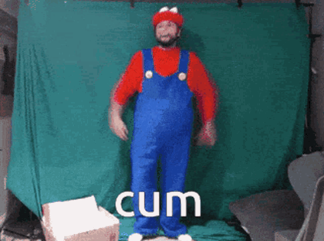 a man in a mario costume is standing in front of a green backdrop with the word cum written in white