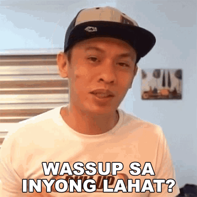 a man wearing a baseball cap and a white shirt says " wassup sa inyong lahat "