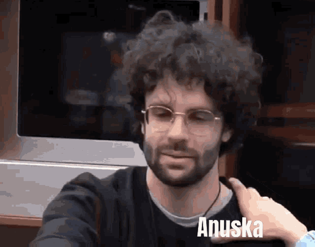 a man with glasses and a beard has the name anuska on his chest