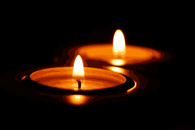 two lit candles in a dark room with the name photography written on the bottom right corner