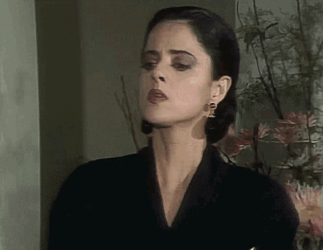 a woman wearing a black jacket and gold earrings looks serious