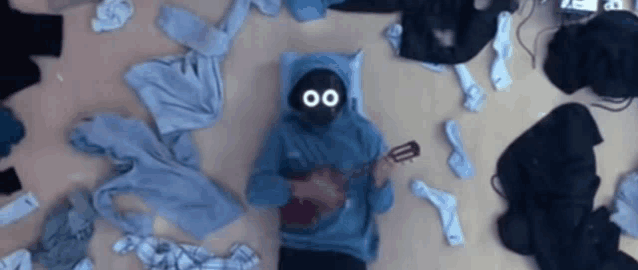 a person laying on the floor playing a guitar with clothes around them