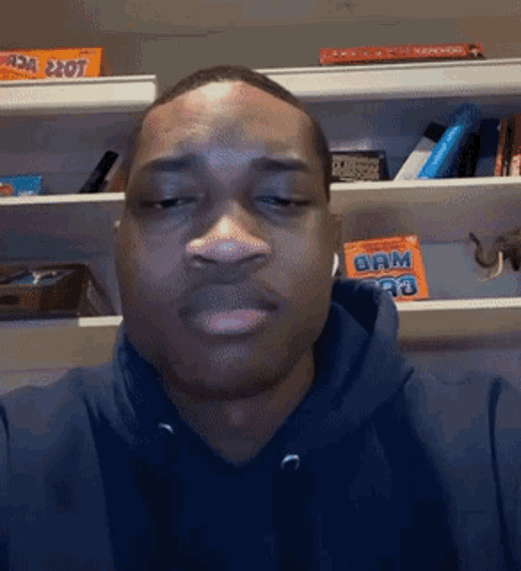 a man wearing a blue hoodie is standing in front of a shelf with a box of foam gum