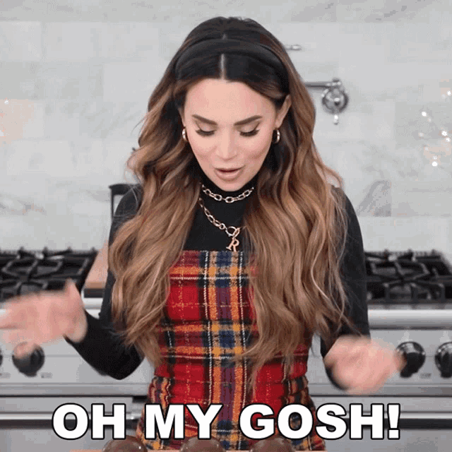 a woman in a plaid dress says oh my gosh in front of a stove