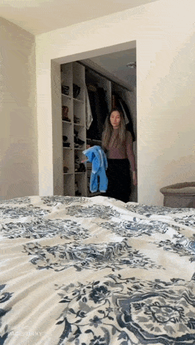 a woman standing in a closet next to a bed with a floral comforter