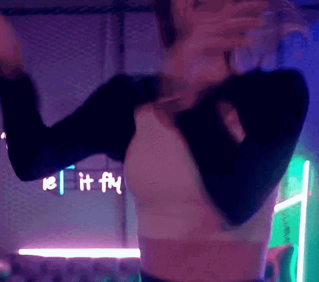 a woman is dancing in front of a neon sign that says ' let it fly '