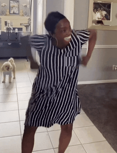 a woman in a striped dress is dancing in a living room with a small dog in the background