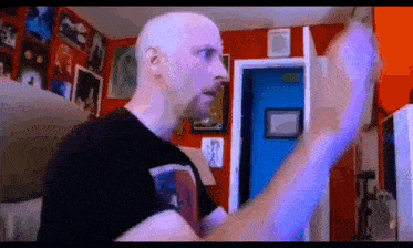 a bald man is standing in a room with a blue door and a red wall .