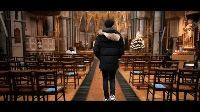 a man in a black jacket is walking down the aisle of an empty church
