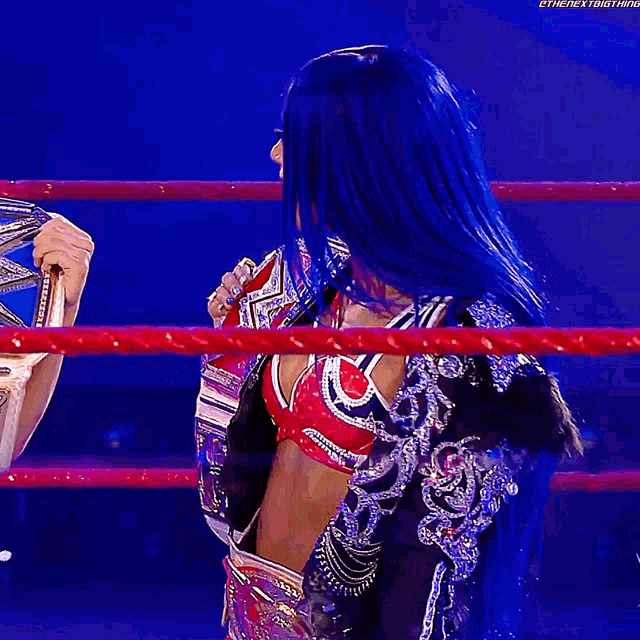 a woman with blue hair is in a wrestling ring holding a belt .