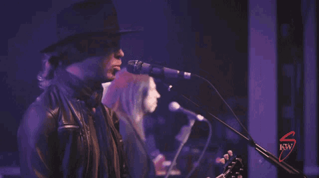 a man singing into a microphone in front of a sign that says ' rw ' on it