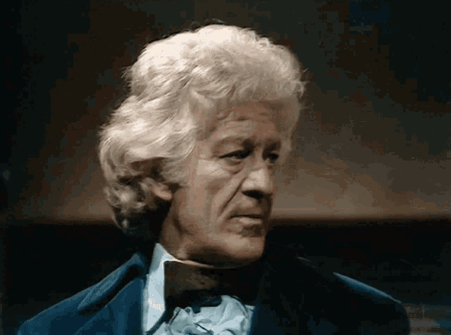 a man with white hair is wearing a blue coat and a bow tie