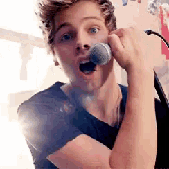 a young man is singing into a microphone and making a funny face .