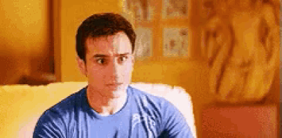 a man is sitting on a couch wearing a blue shirt and looking at the camera .