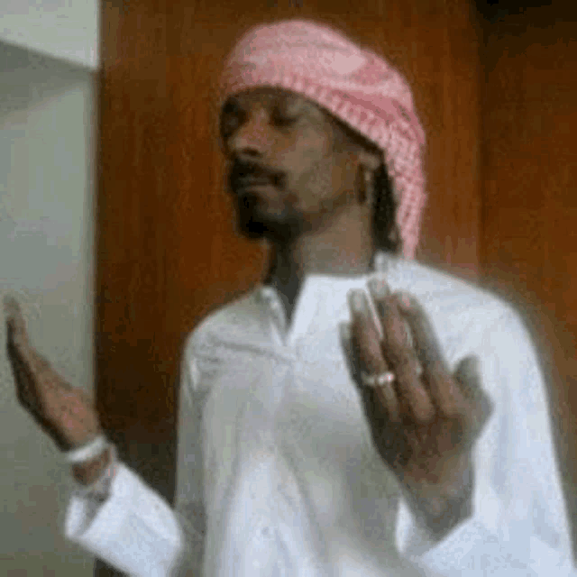 snoop dogg is wearing a pink head scarf and a white shirt while smoking a cigarette .