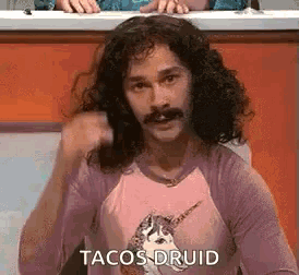 a man with long hair and a mustache is wearing a pink shirt with a unicorn on it .