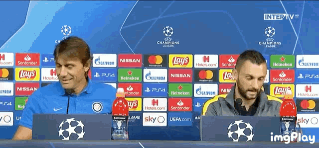 two men sitting in front of a champions league advertisement