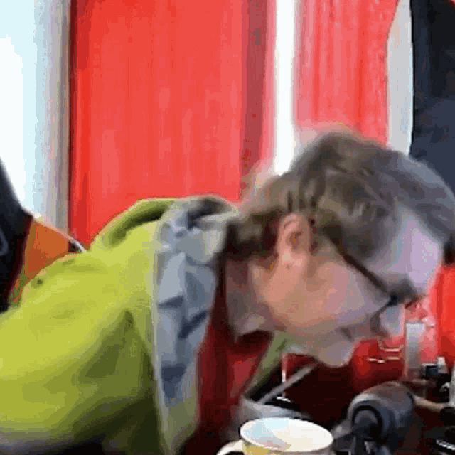 a man in a green jacket is sitting at a table with a cup of coffee in front of him