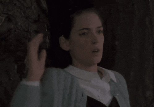 a woman in a blue cardigan and white shirt is standing in a dark room .
