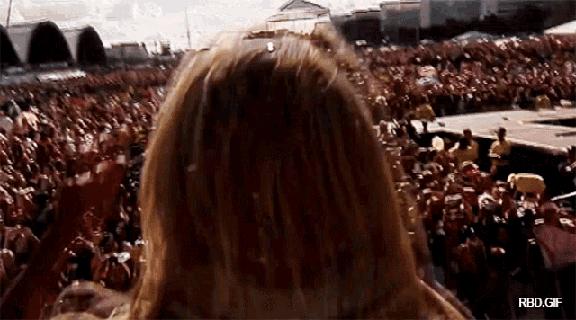 a woman stands in front of a crowd at a concert with rbd.gif below her