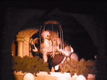 a skeleton is sitting in a cage with a bird behind it