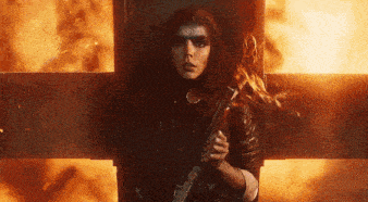 a woman is holding a gun in front of a fire cross