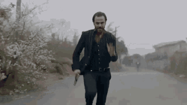 a man in a suit and vest is running down a street with a gun in his hand .