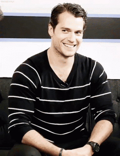 a man wearing a black and white striped shirt is smiling while sitting on a couch
