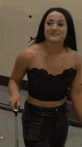 a woman in a black crop top and leather pants is holding a suitcase and smiling .
