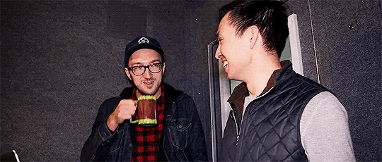 two men are standing next to each other in a room drinking from mugs .