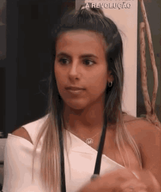 a woman wearing a white top and a necklace is sitting in a room .
