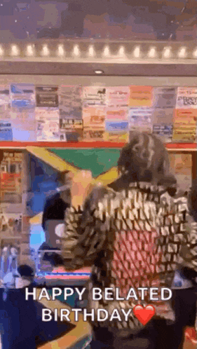 a woman is dancing in a room with a sign that says happy belated birthday .